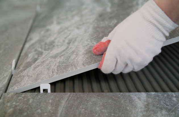 Carreleur équipé de gants qui pose un carreau de carrelage sur du mortier colle