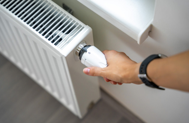Réglage manuel de la vanne thermostatique d’un radiateur blanc installé sous une fenêtre.
