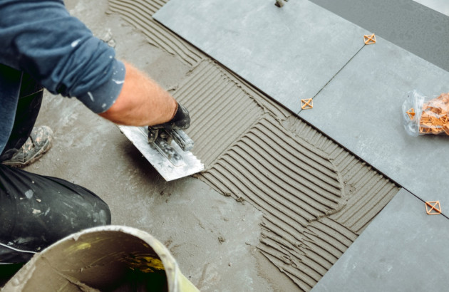 Artisan carreleur qui utilise un truelle pour étaler du mortier colle lors de la pose de carrelage