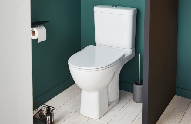 WC à poser compact dans un petit espace, mur bleu, porte-rouleau et brosse WC.