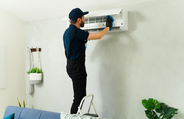 professionnel qui nettoie l'intérieur d'un climatiseur mural blanc avec un chiffon bleu effectuant un entretien de l'appareil