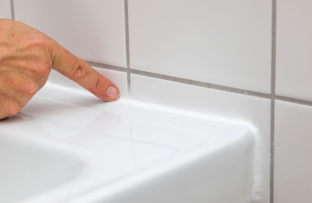 Homme qui appuie son doigt sur un joint en silicone entre un lavabo et un mur en carrelage