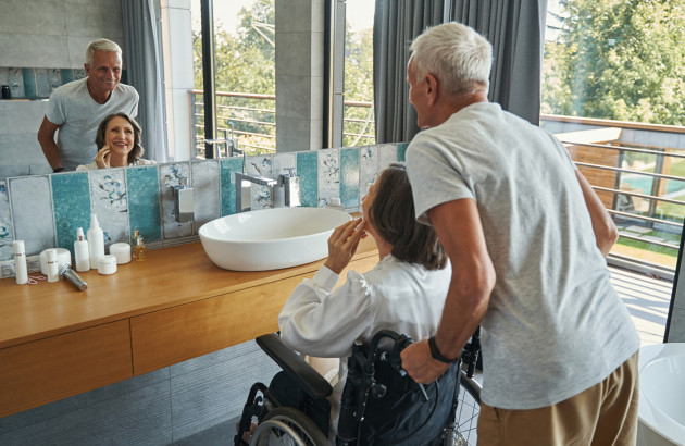 Homme agé qui pousse sa femme agée en fauteuil roulant dans leur salle de bains