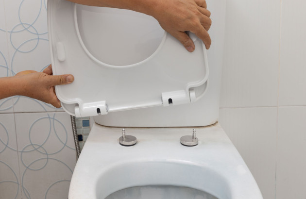 Personne qui installe un abattant de toilettes sur les fixations prévues à cet effet