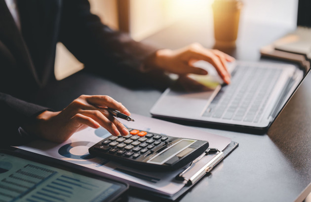 personne utilisant une calculatrice et un ordinateur portable avec des documents financiers et des graphiques sur le bureau