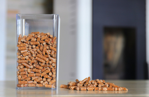 Pellets de bois dans un récipient en plastique avec un poele à granulé en arrière plan