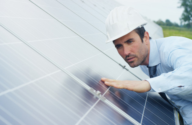 Homme en chemise et cravate avec un casque de chantier qui touche une installation de panneau solaire dans le but de vérifier le fonctionnement