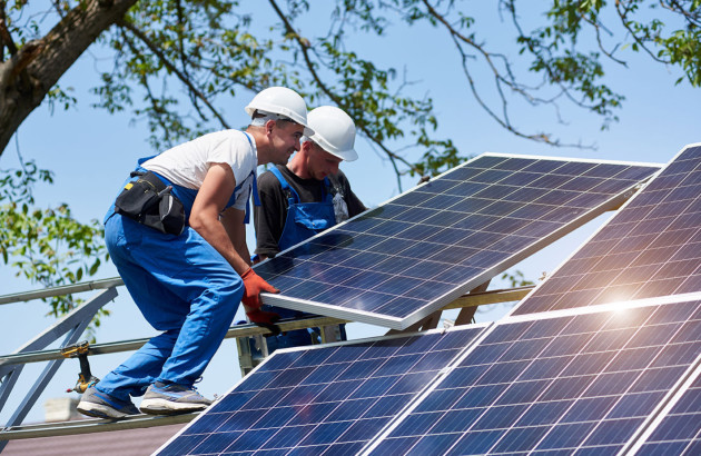 Deux installateurs posant un panneau solaire sur une structure de fixation.