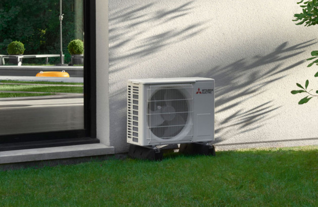 pompe à chaleur air-air de marque Mitsubishi Electric placée sur une pelouse verte et sur le mur d'une maison