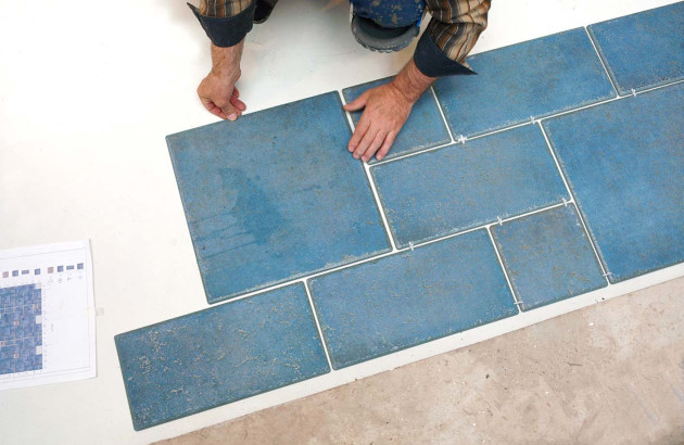 Personne qui pose des carreaux de carrelage bleus