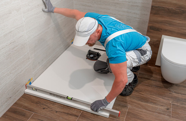 Artisan posant un receveur de douche avec niveau à bulle dans salle de bains