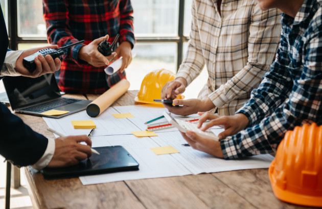 Réunion de chantier avec plans, calculs et équipements de protection pour préparer des travaux de rénovation.