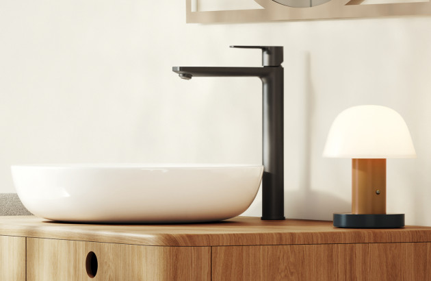 Robinet de salle de bains noir mat posé sur un meuble en bois clair avec vasque blanche contemporaine.