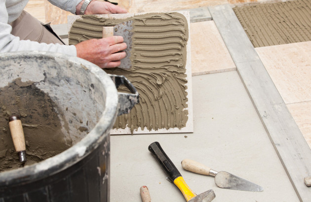 Artisan carreleur qui étale du mortier colle sur un carreau de carrelage