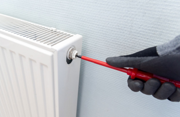 Homme avec des gants et muni d'un tournevis qui va purger un radiateur