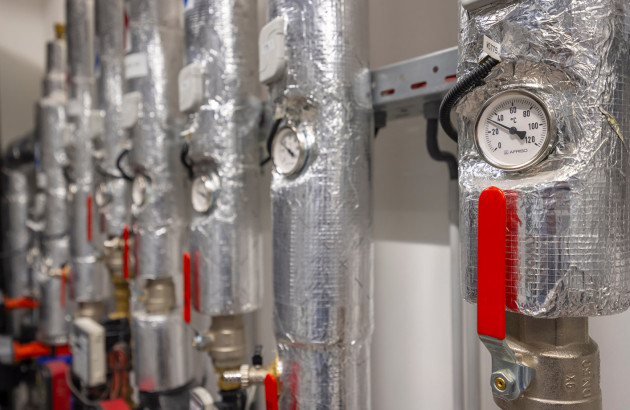 Plusieurs tuyaux de chauffage avec des manomètres de pression, calorifugés avec des feuilles qui s'apparentent à de l'aluminium