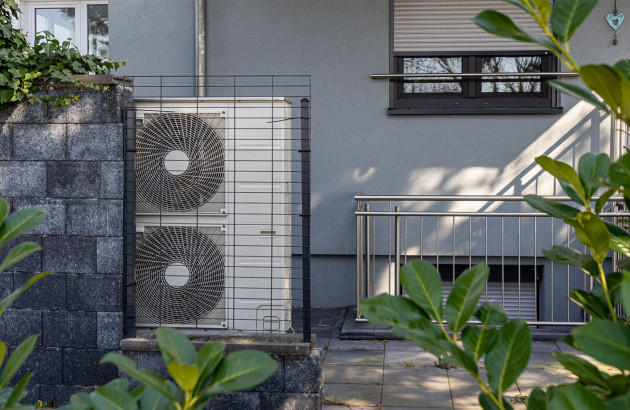 Pompe à chaleur avec double ventilateur installée à l’extérieur d’une habitation et protégée par une grille.