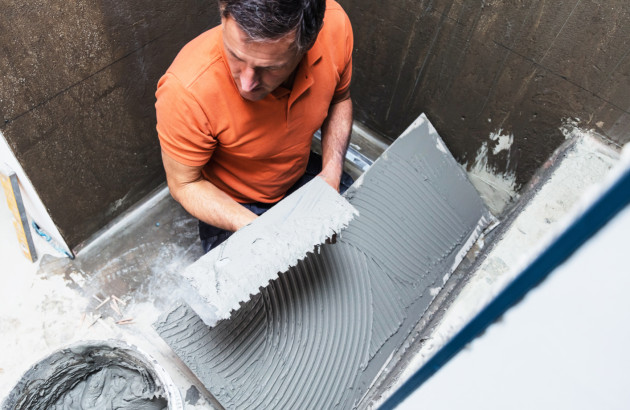 Application de colle carrelage pour préparer le support avant pose du receveur de douche.