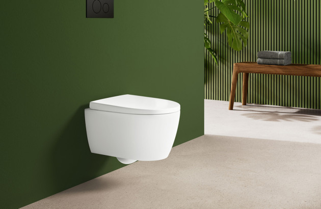 WC suspendu blanc sur mur vert avec commande double chasse et banc bois en arrière-plan.