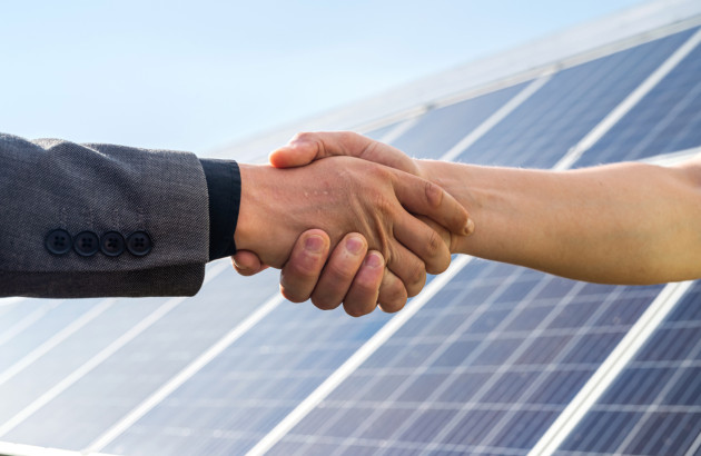 Poignée de main devant des panneaux solaires photovoltaïques symbolisant un accord pour un projet d'installation solaire.