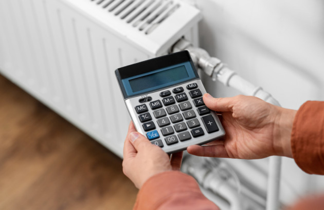 Personne utilisant une calculatrice devant un radiateur pour estimer les dépenses de chauffage.