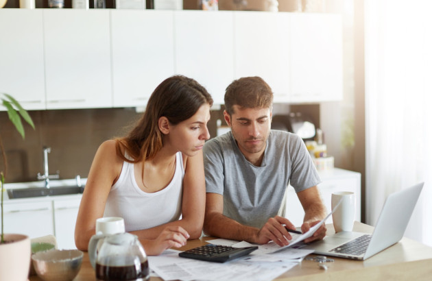 Jeune couple qui se renseigne sur les aides financières sur un ordinateur et des documents papiers