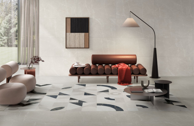 Salon minimaliste avec canapé d’angle beige, grandes baies vitrées et carrelage effet béton gris au sol.