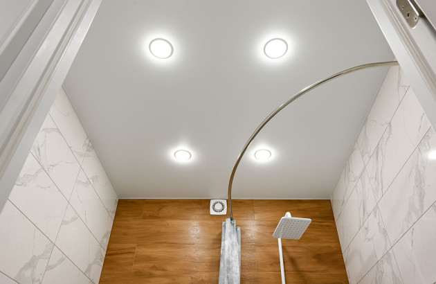 Spot encastré au dessus d'une douche dans une salle de bain au mur marbre blanc et bois