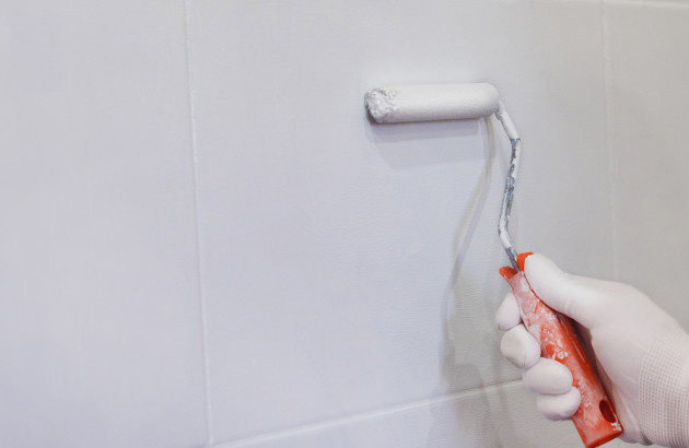 Personne qui repeint un carreau de carrelage en blanc avec un petit rouleau de peinture