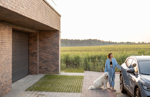 Femme qui recharge sa voiture électrique depuis sa maison, accompagnée de son chien 