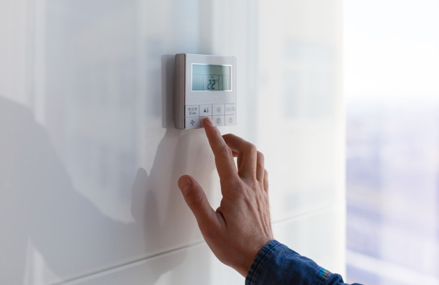 Main réglant la température d’un système de climatisation à l’aide d’un thermostat mural numérique