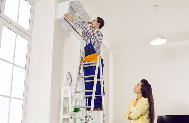 Installateur posant une climatisation murale chez un particulier avec une échelle.