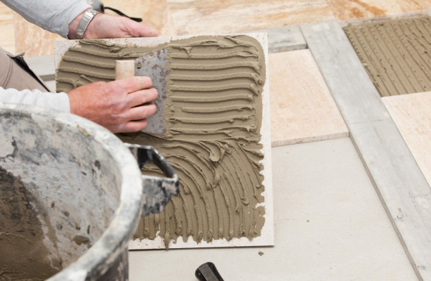 application de mortier-colle sur une dalle de carrelage avec une spatule crantée