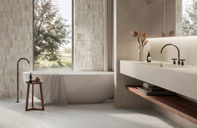 Salle de bains lumineuse avec baignoire îlot blanche, carrelage mural beige brillant et meuble vasque suspendu.