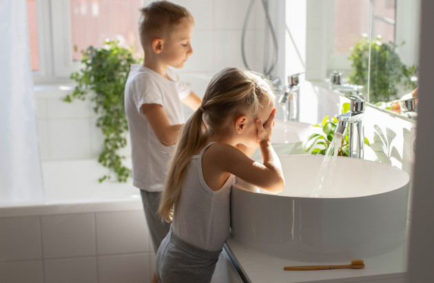 Deux enfants faisant leur toilette devant une grande vasque dans une salle de bains lumineuse.