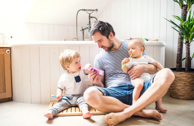 Père accompagné de deux jeunes enfants dans une salle de bains familiale équipée d’une baignoire.