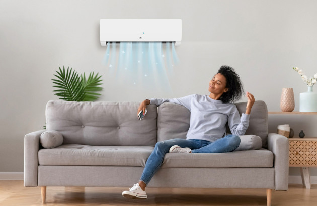 femme détendue assise sur un canapé profitant de l'air frais diffusé par un climatiseur mural blanc dans le salon