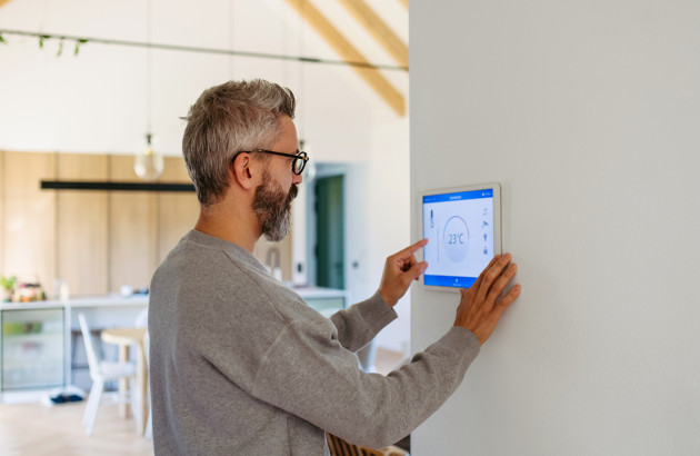 Homme ajustant la température sur un thermostat connecté pour piloter son chauffage ou sa climatisation.