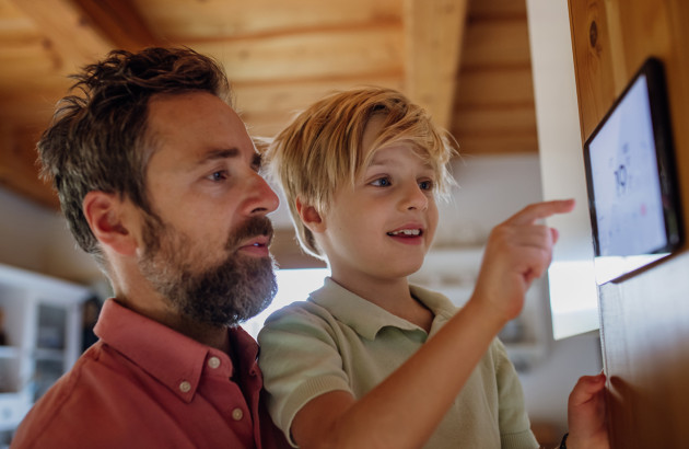 Père et son fils qui règlent le thermostat digital d'un système de chauffage