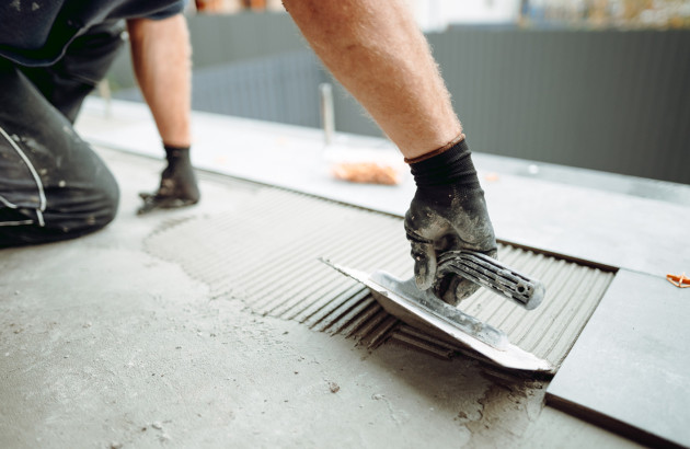 Homme avec une taloche qui étale du mortier colle sur des carreaux de carrelage