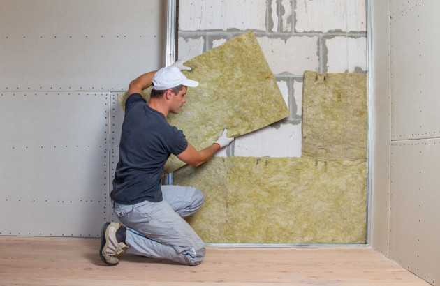 Homme qui installe des plaques isolantes sur un mur de maison à l'intérieur