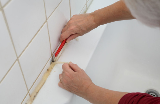 Personne qui utilise un cutter pour retirer un vieux joint de silicone