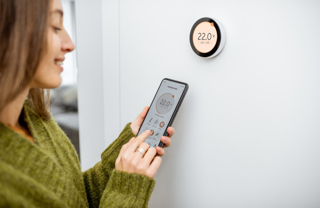 Femme qui règle la température de son logement avec son téléphone et un thermostat connecté