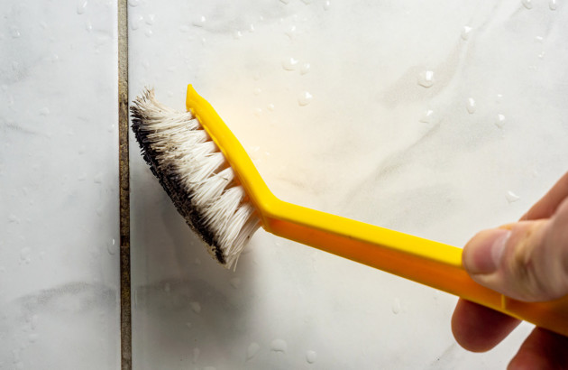 Personne qui frotte les joints de carrelage de salle de bains avec une brosse