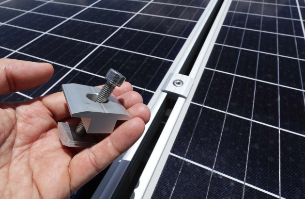 Main qui tient une pièce qui permet de fixer des panneaux solaires sur les rails de fixation