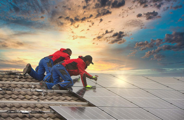 Deux ouvriers sur un toit de maison qui vissent des panneaux solaires au rails de support