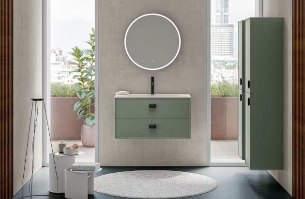 Meuble sous vasque vert sauge suspendu associé à une colonne de rangement et un miroir rond rétroéclairé dans un intérieur contemporain.
