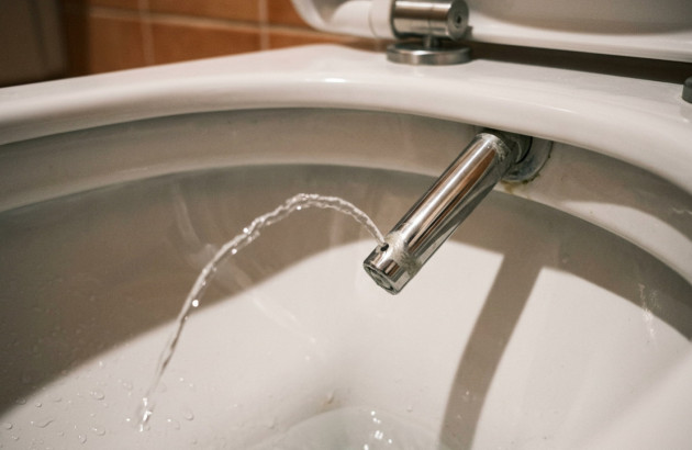 Gros plan sur la douchette intégrée d’un WC lavant diffusant un jet d’eau.