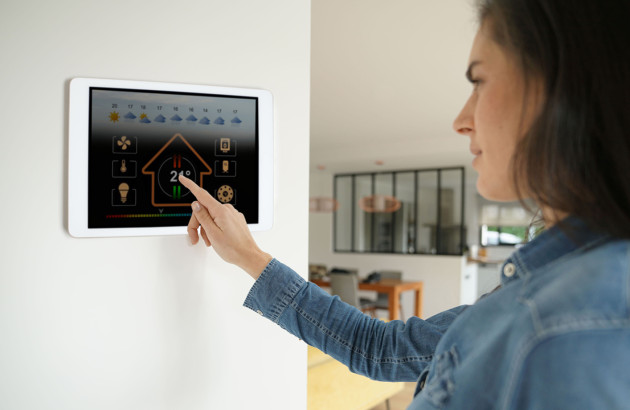 Thermostat mural connecté réglé par une personne pour piloter la climatisation.