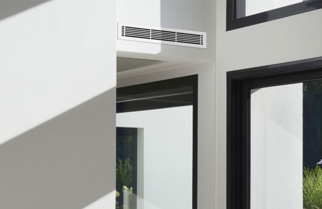 grille de climatisation sur un mur blanc, encadrement de porte et fenêtre noir visible sur le côté droit de l'image
